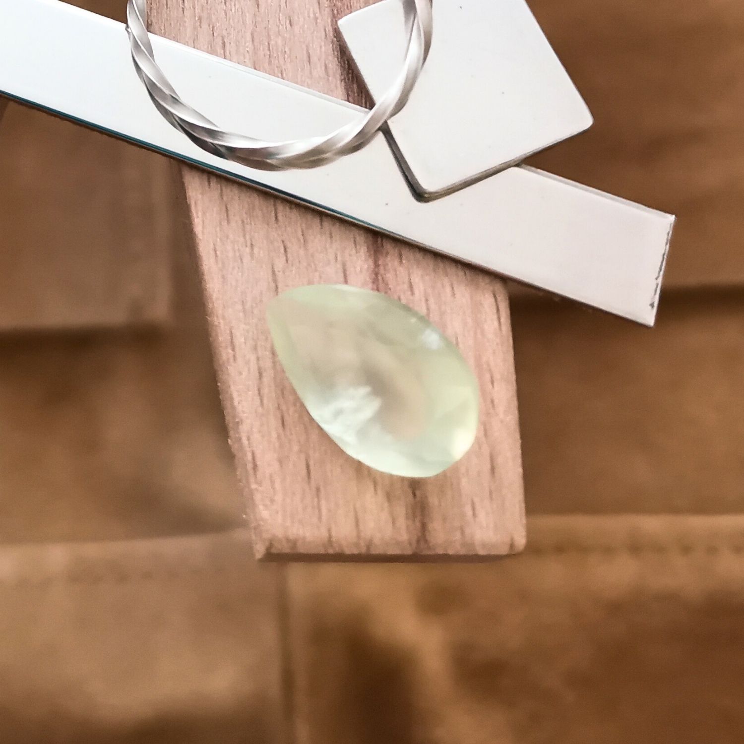 The yellow-green prehnite teardrop displayed on a jewellers bench peg with some sterling silver sheet and wire.
