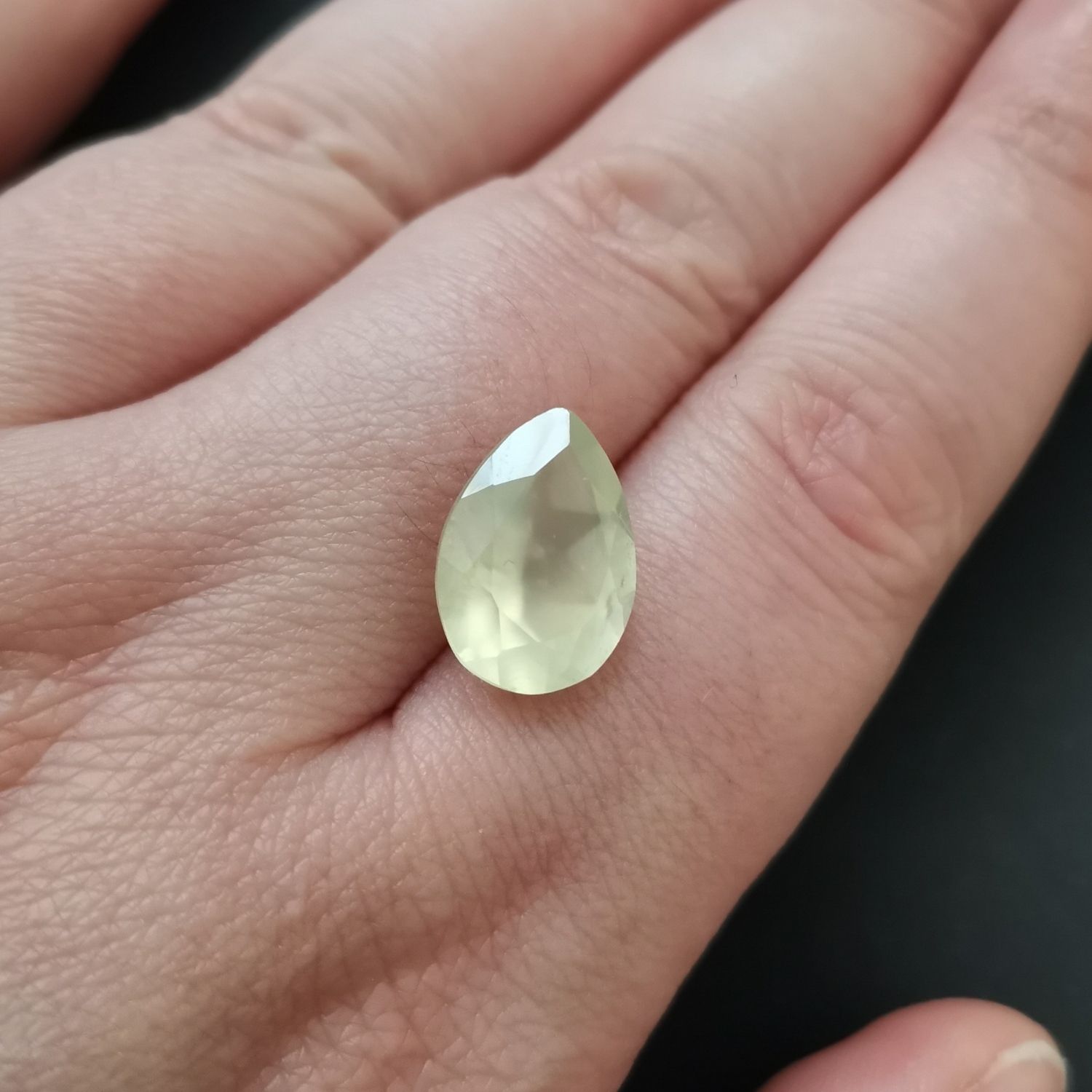 The faceted teardrop prehnite resting on a hand to show size and colour.