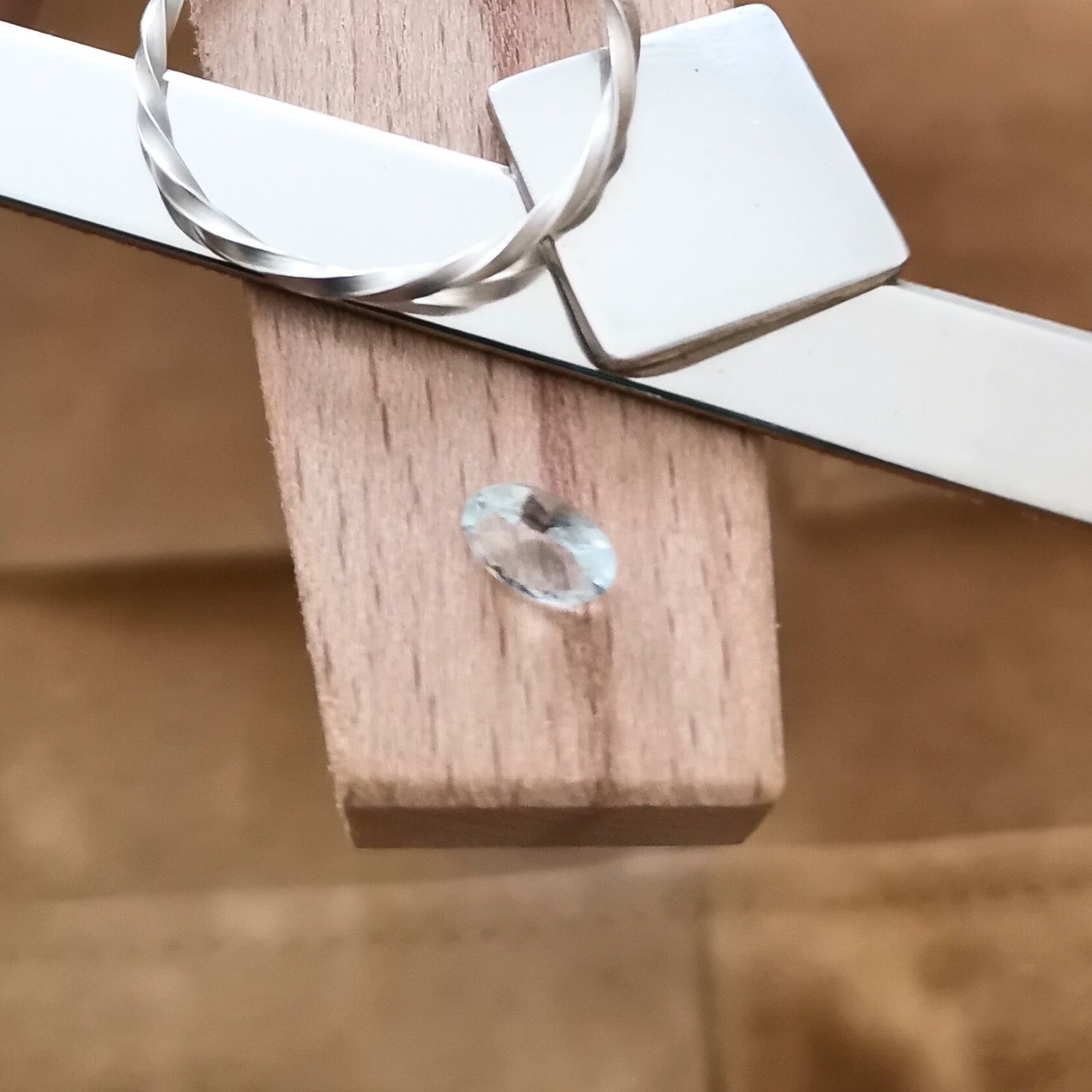 The colourless goshenite oval displayed on a jewellers bench peg with some sterling silver sheet and wire.