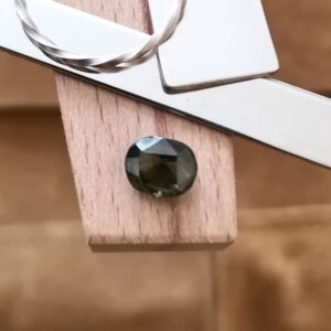 The olive green zircon displayed on a jewellers bench peg with some sterling silver sheet and wire.