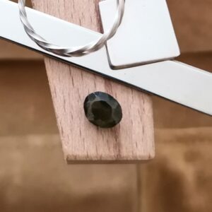 The olive green zircon oval displayed on a jewellers bench peg with some sterling silver sheet and wire.