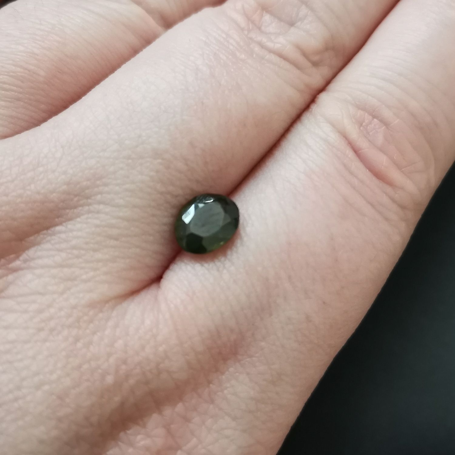 The faceted oval zircon resting on a hand to show size and colour.