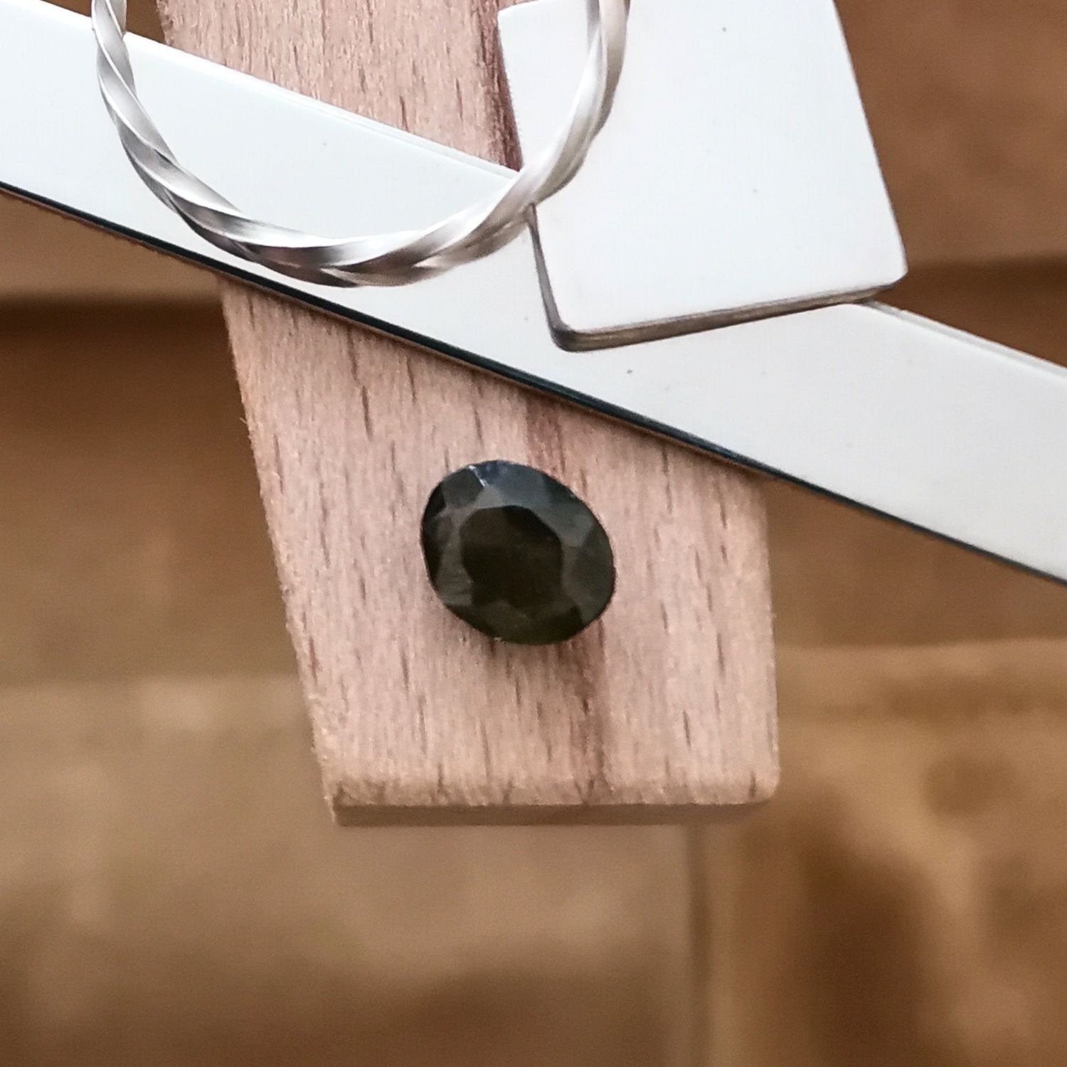 The olive green zircon oval displayed on a jewellers bench peg with some sterling silver sheet and wire.