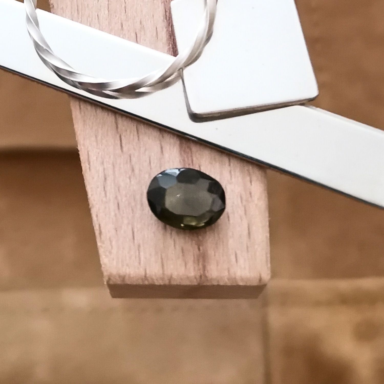 The olive green zircon oval displayed on a jewellers bench peg with some sterling silver sheet and wire.