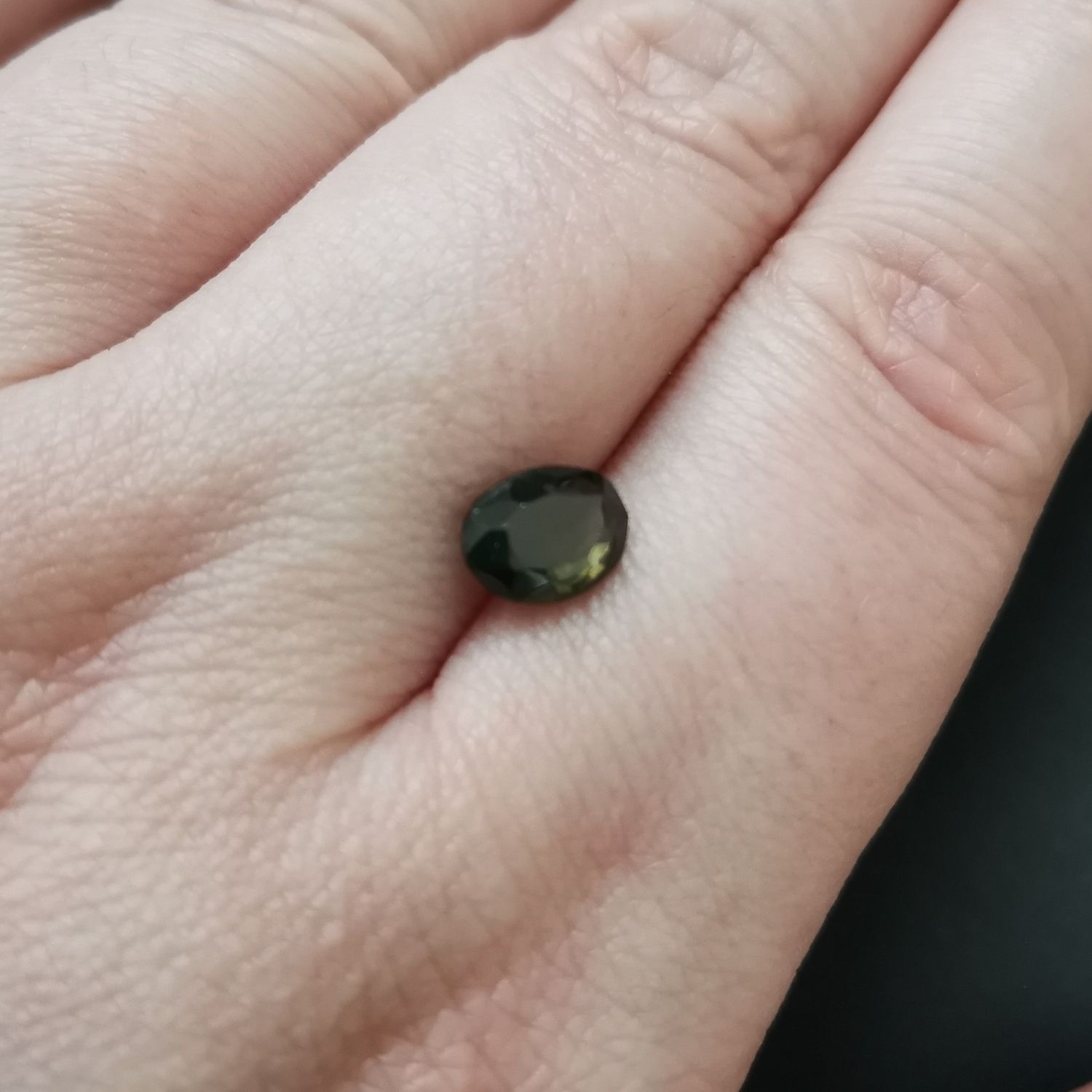 The faceted oval zircon resting on a hand to show size and colour.