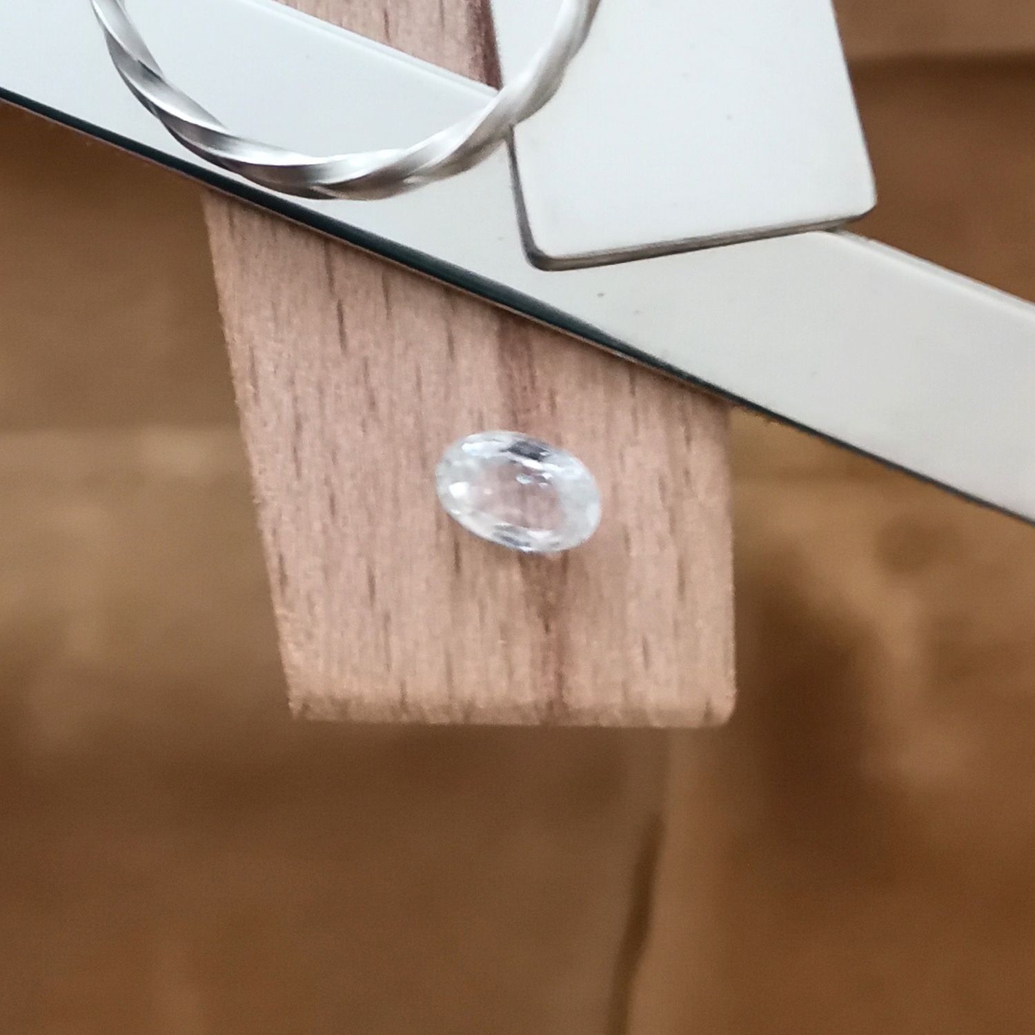 The white zircon oval displayed on a jewellers bench peg with some sterling silver sheet and wire.