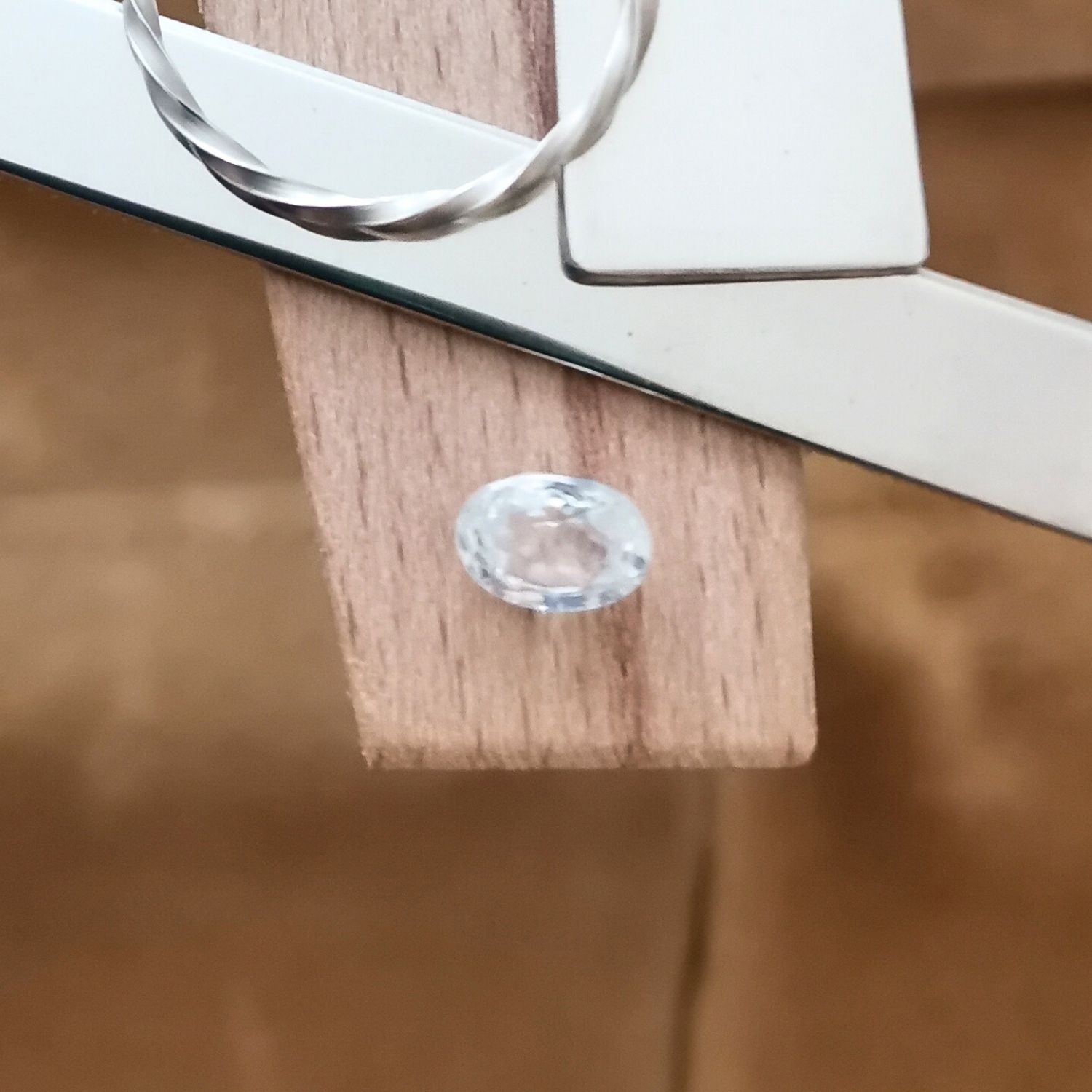 The colourless zircon oval displayed on a jewellers bench peg with some sterling silver sheet and wire.