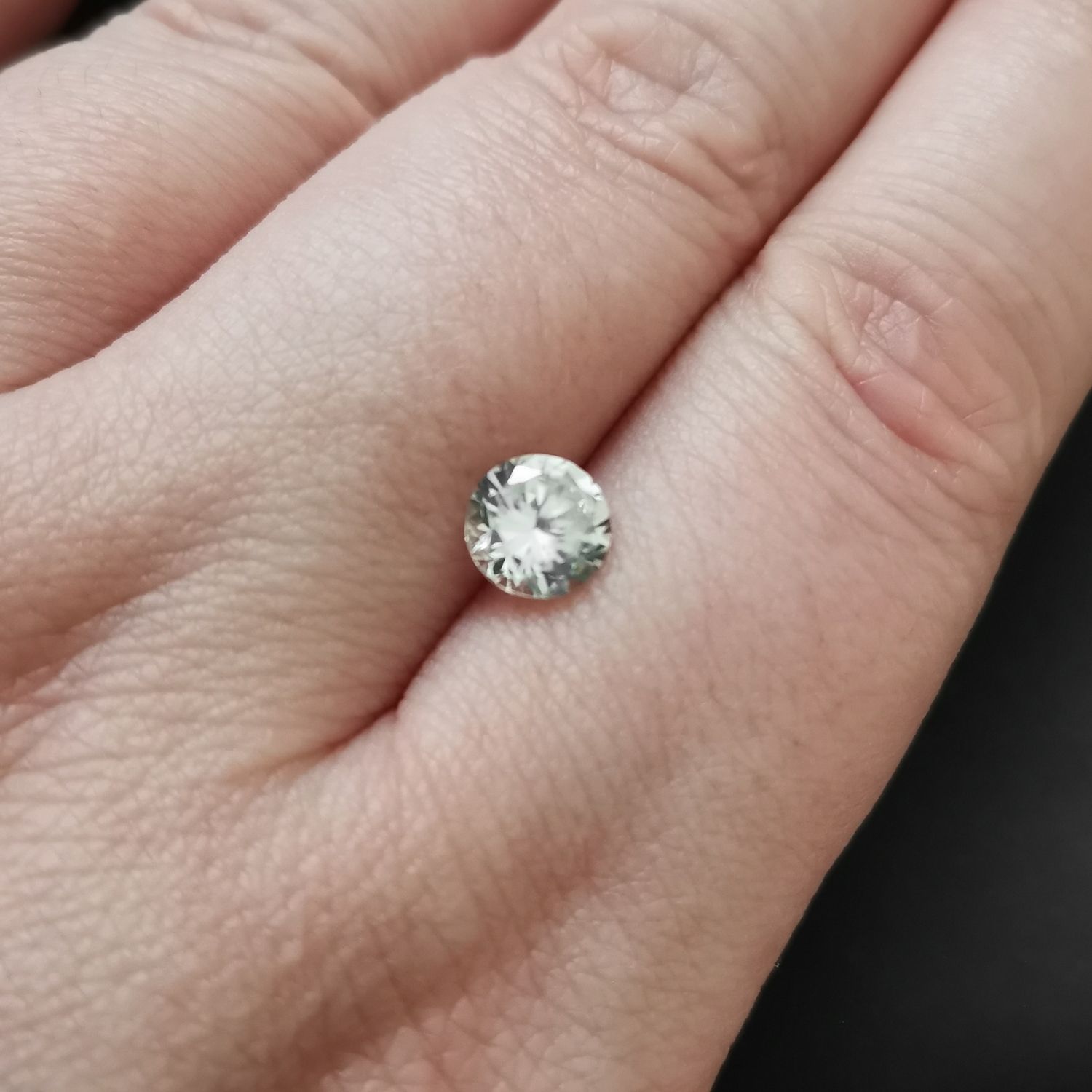 The faceted round zircon resting on a hand to show size and colour.