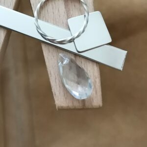 The pale grey smoky quartz teardrop displayed on a jewellers bench peg with some sterling silver sheet and wire.