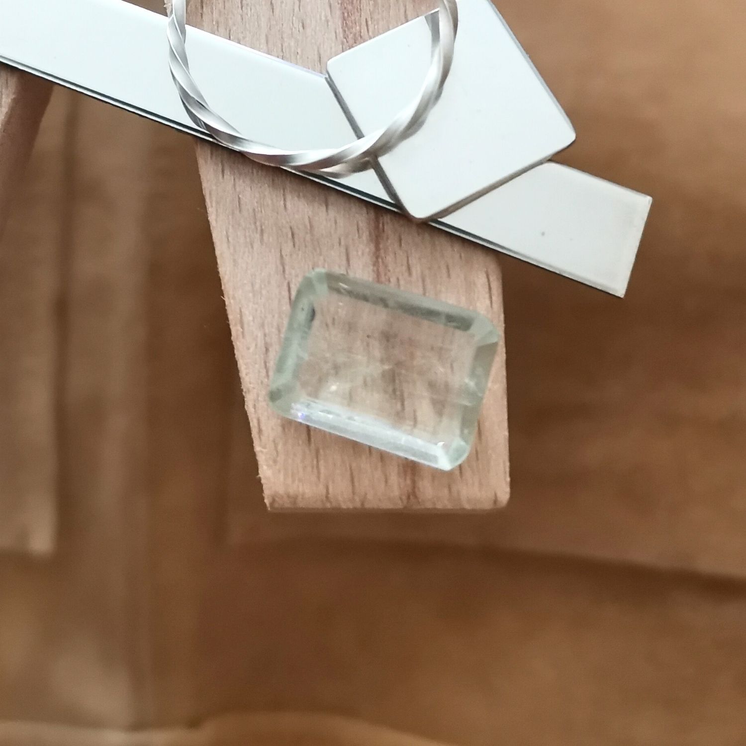 The yellowish green prasiolite rectangle displayed on a jewellers bench peg with some sterling silver sheet and wire.