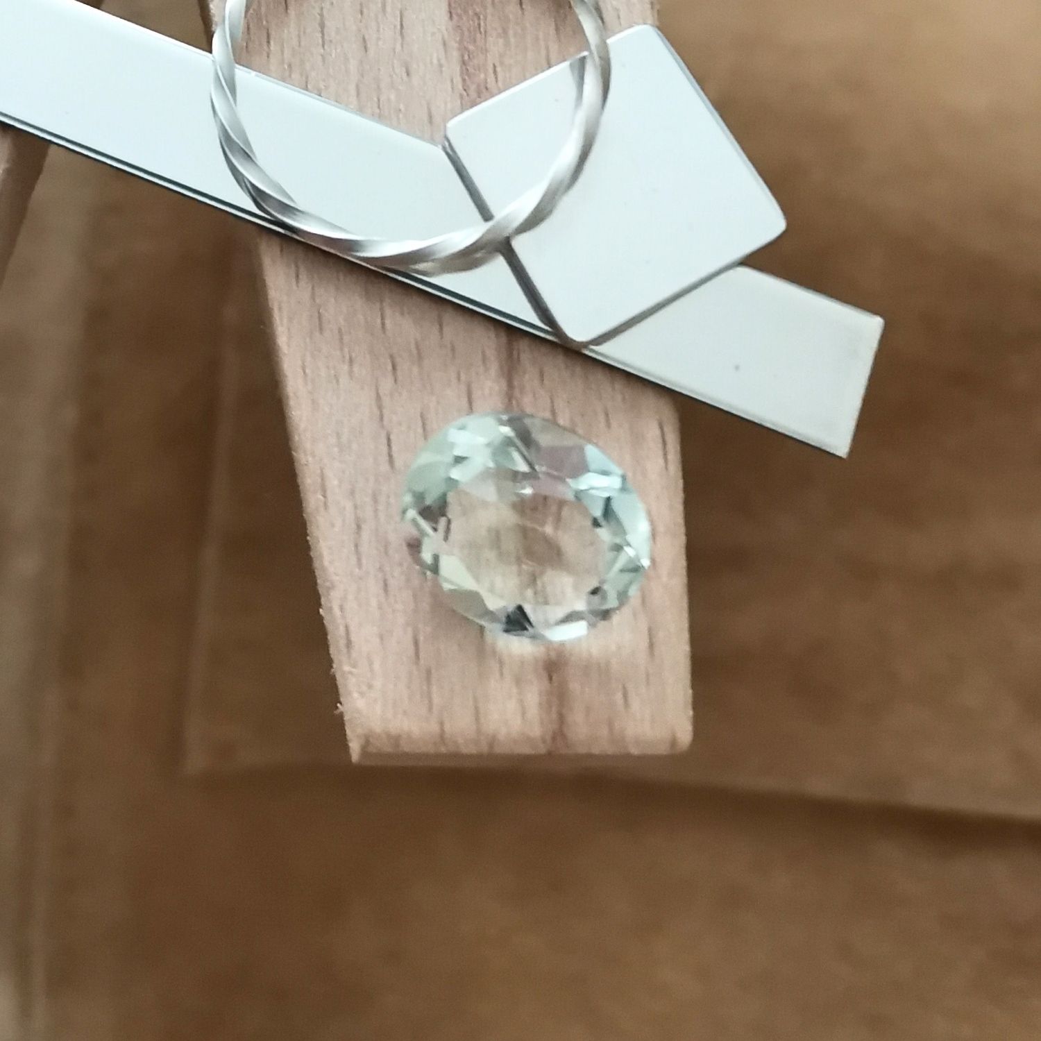 The yellowish green prasiolite oval displayed on a jewellers bench peg with some sterling silver sheet and wire.