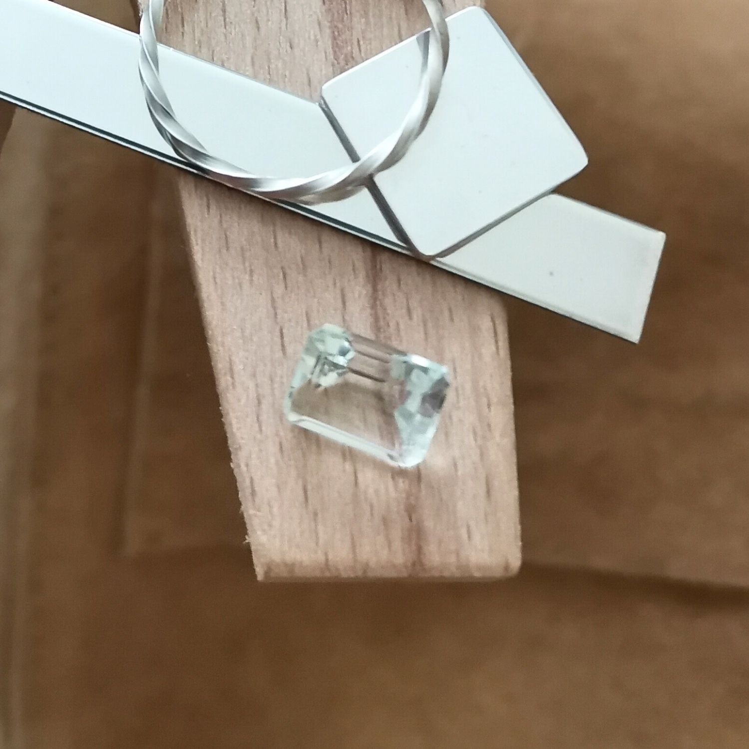 The yellowish green prasiolite rectangle displayed on a jewellers bench peg with some sterling silver sheet and wire.