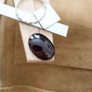 The reddish purple garnet cabochon displayed on a jewellers bench peg with some sterling silver sheet and wire.