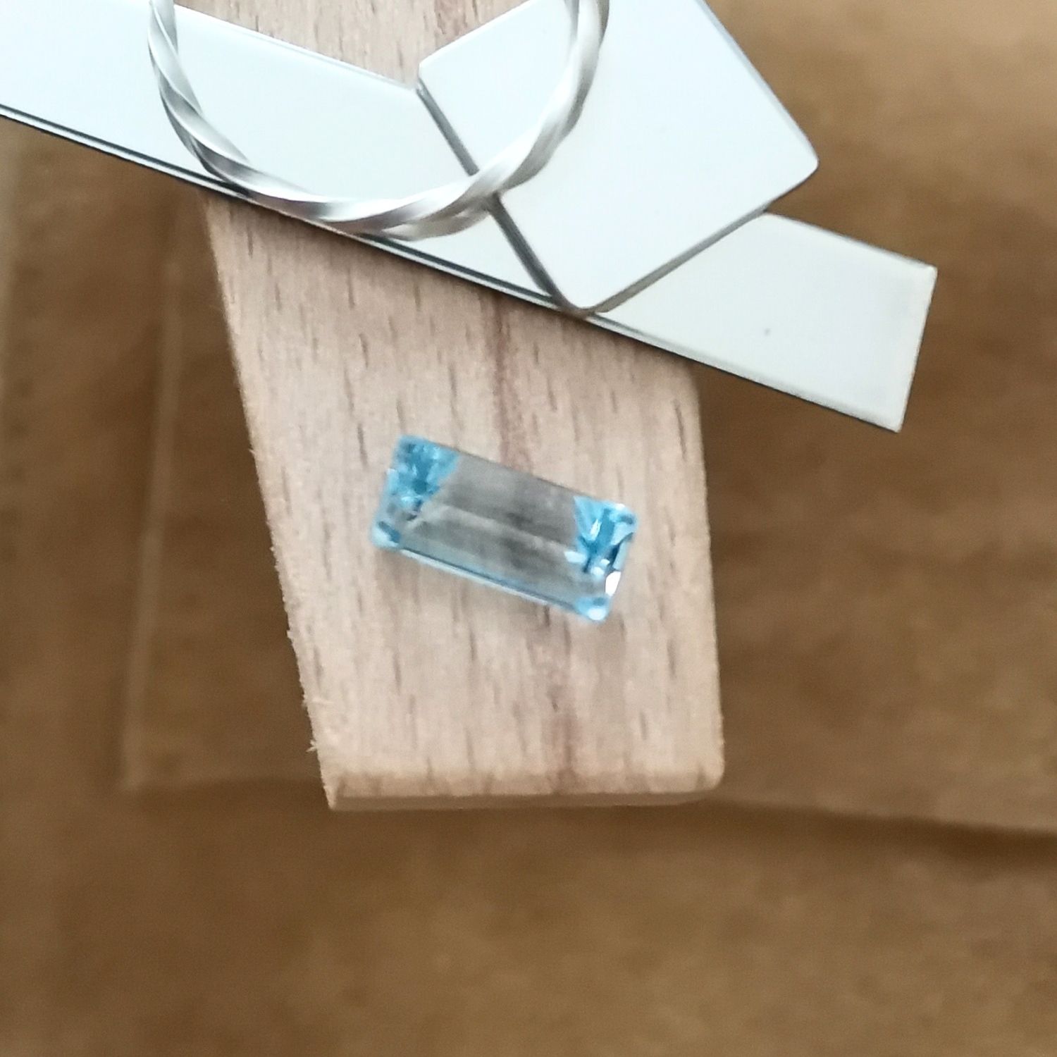 The lab grown blue spinel rectangle displayed on a jewellers bench peg with some sterling silver sheet and wire.