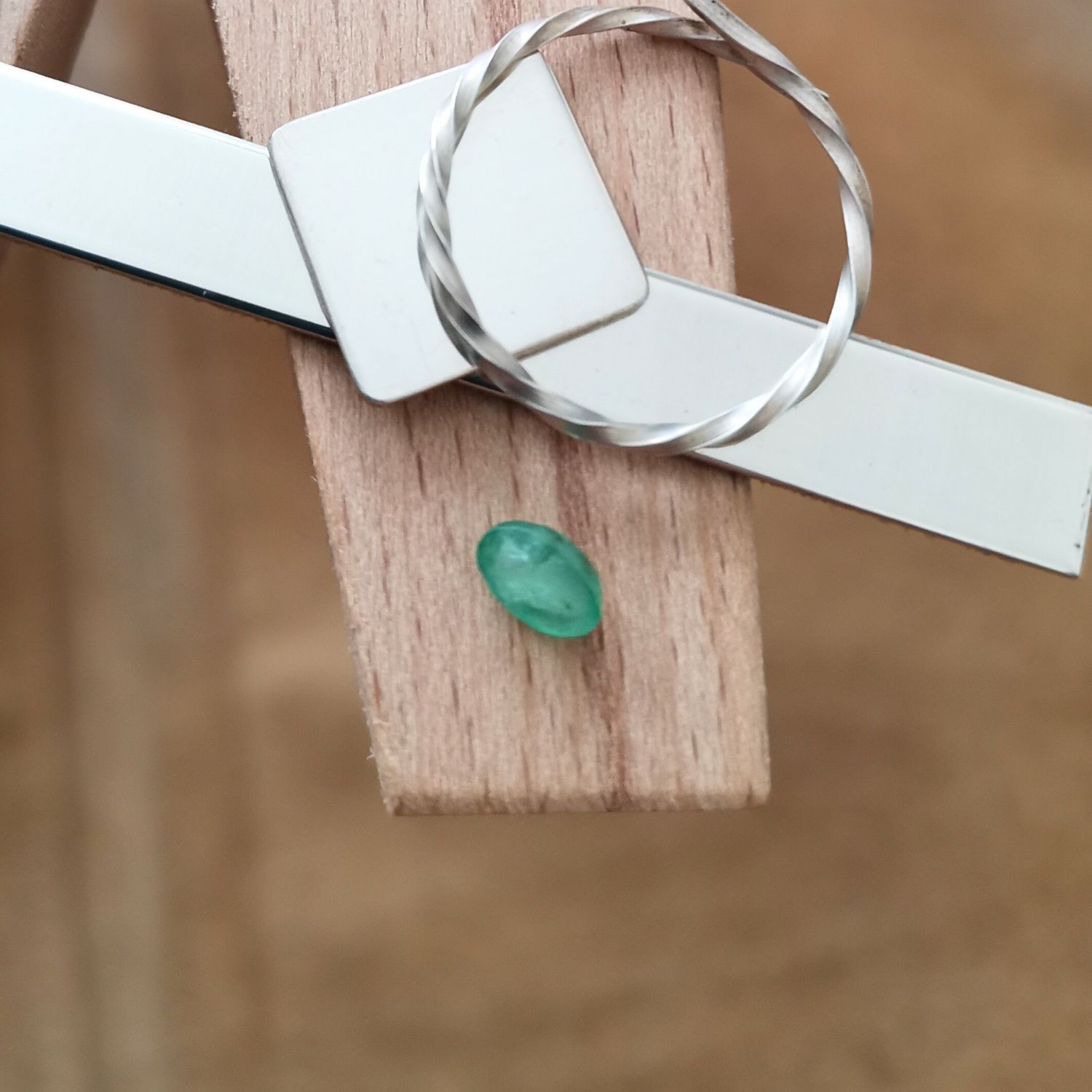 The green emerald oval displayed on a jewellers bench peg with some sterling silver sheet and wire.