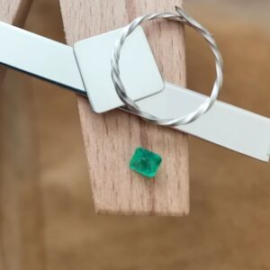 The bright green emerald square displayed on a jewellers bench peg with some sterling silver sheet and wire.