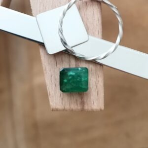 The large green emerald rectangle displayed on a jewellers bench peg with some sterling silver sheet and wire.