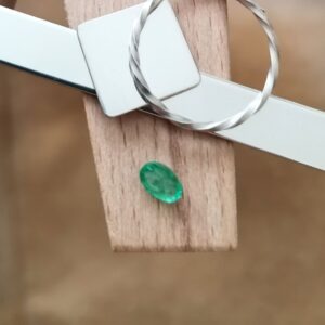 The bright green emerald oval displayed on a jewellers bench peg with some sterling silver sheet and wire.
