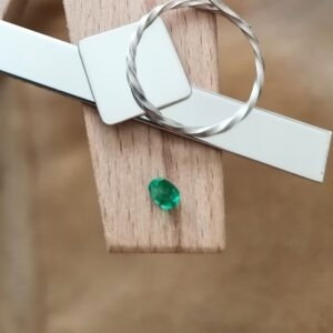 The vibrant green emerald oval displayed on a jewellers bench peg with some sterling silver sheet and wire.