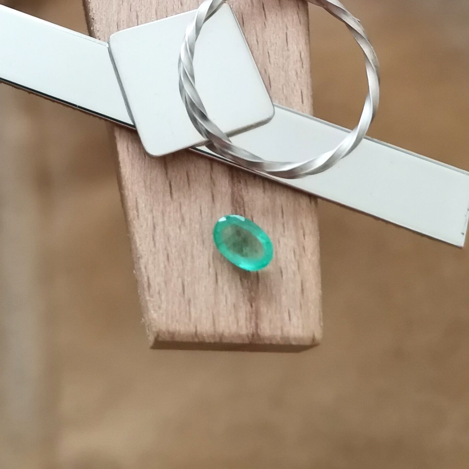 The green emerald oval displayed on a jewellers bench peg with some sterling silver sheet and wire.