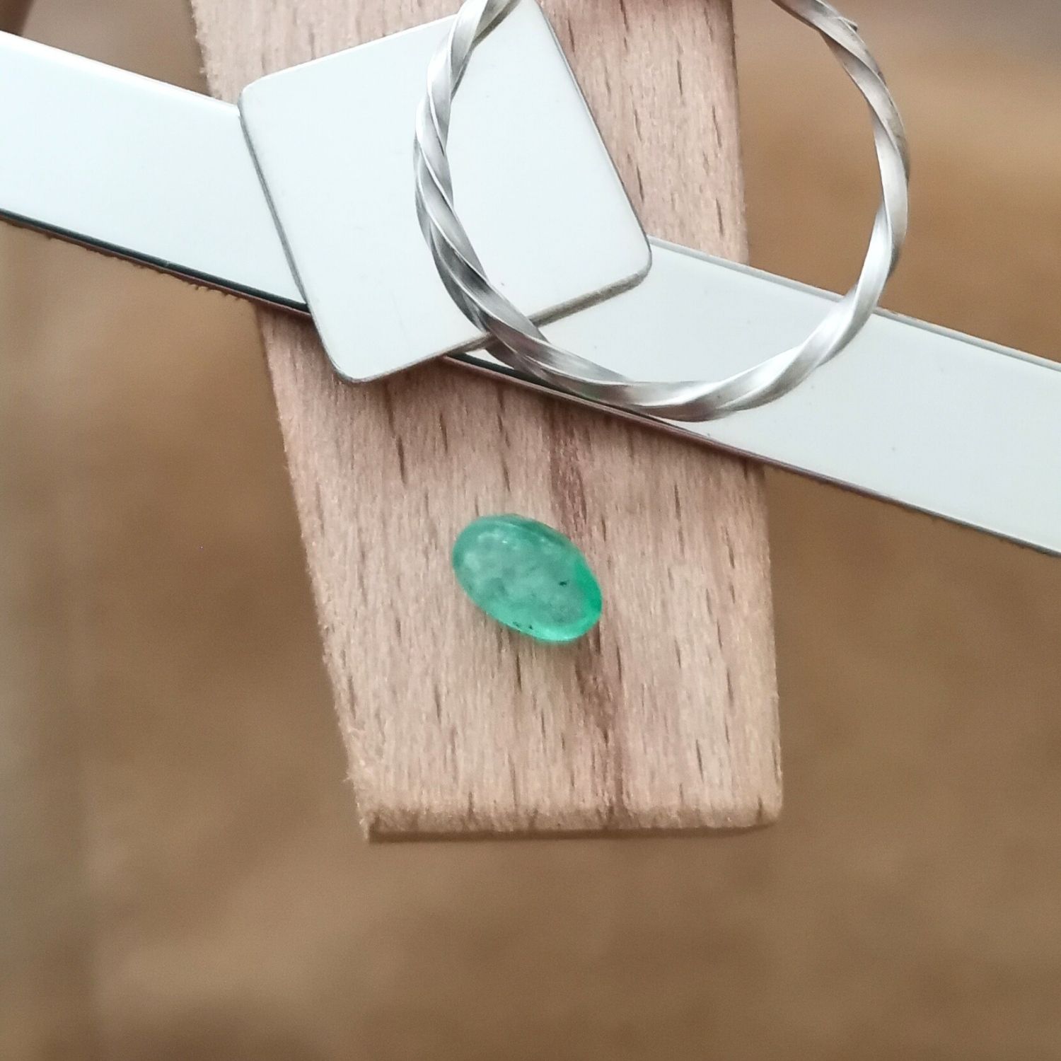 The green emerald oval displayed on a jewellers bench peg with some sterling silver sheet and wire.
