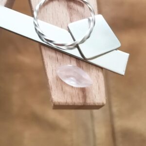 The pale pink rose quartz marquise displayed on a jewellers bench peg with some sterling silver sheet and wire.