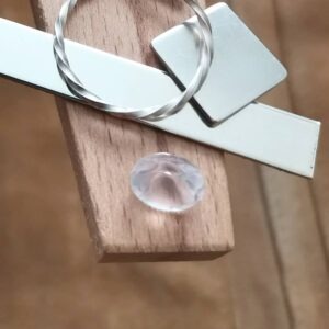 The pale pink rose quartz oval displayed on a jewellers bench peg with some sterling silver sheet and wire.