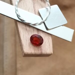 The oval orange hessonite garnet displayed on a jewellers bench peg with some sterling silver sheet and wire.