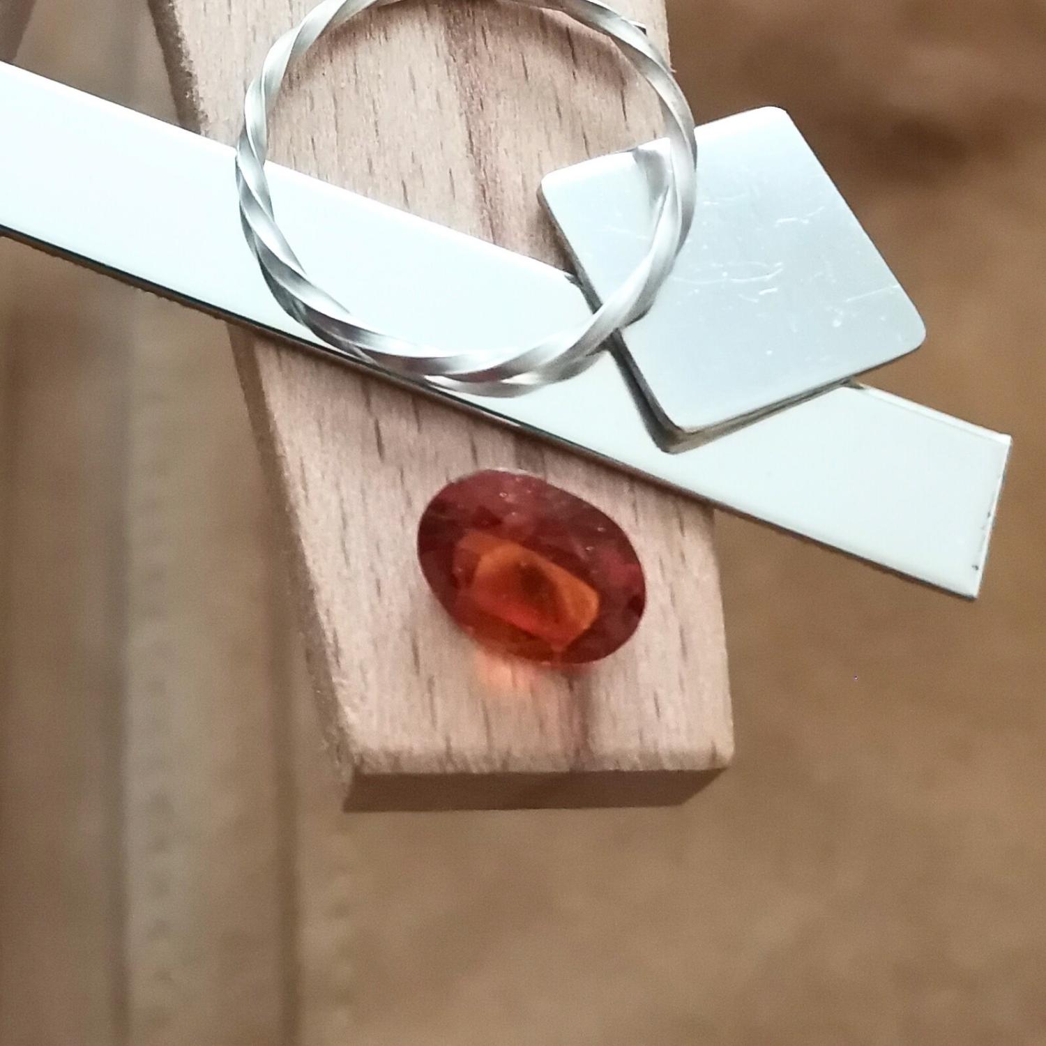 The oval orange hessonite garnet displayed on a jewellers bench peg with some sterling silver sheet and wire.