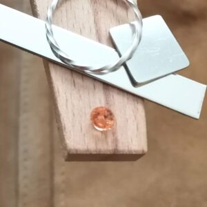 The round orage mali garnet displayed on a jewellers bench peg with some sterling silver sheet and wire.