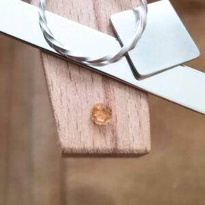 The round golden yellow hessonite garnet displayed on a jewellers bench peg with some sterling silver sheet and wire.