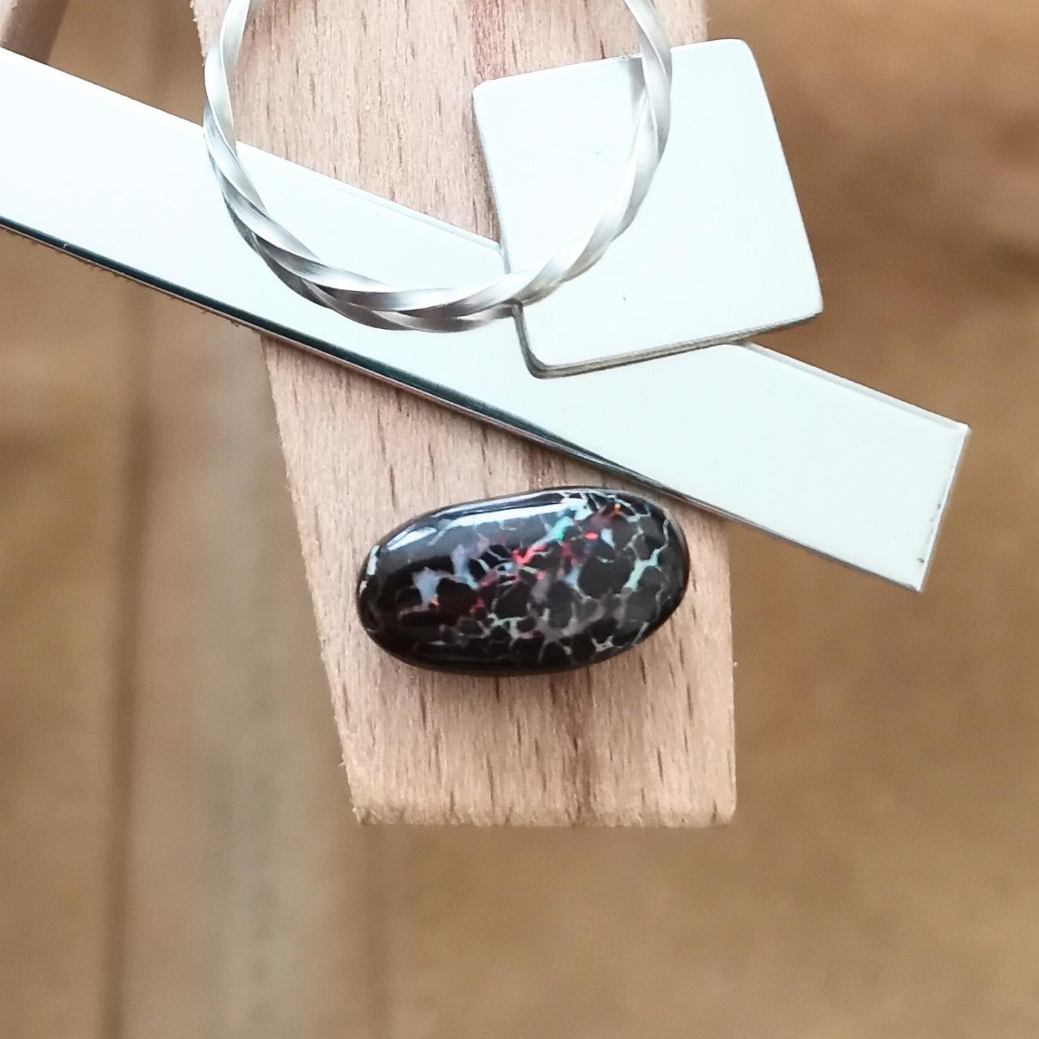 The small free-form boulder opal displayed on a jewellers bench peg with some sterling silver sheet and wire.