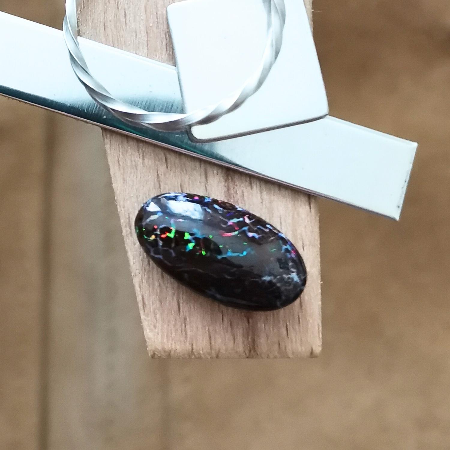 The small free-form boulder opal displayed on a jewellers bench peg with some sterling silver sheet and wire.