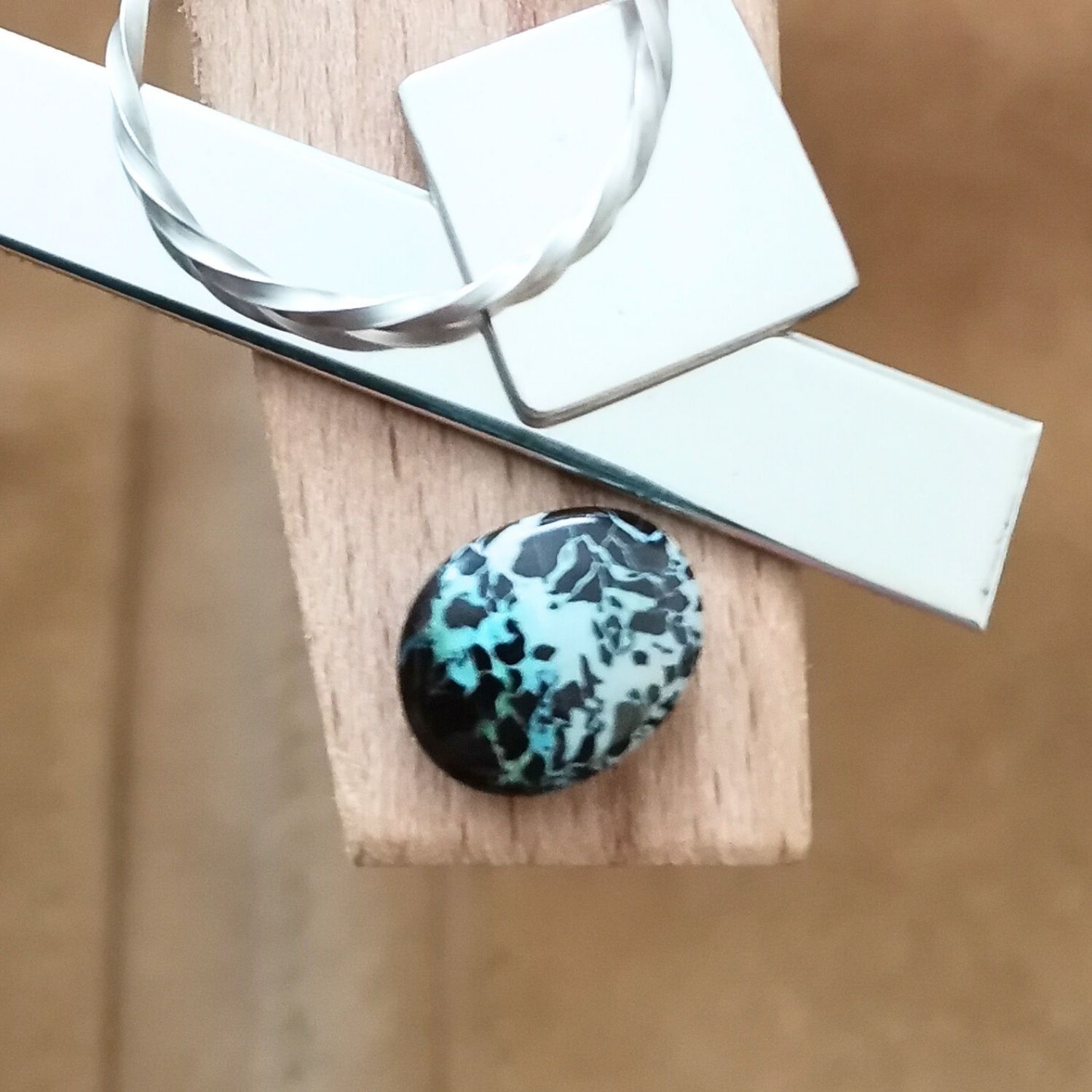 The small free-form boulder opal displayed on a jewellers bench peg with some sterling silver sheet and wire.