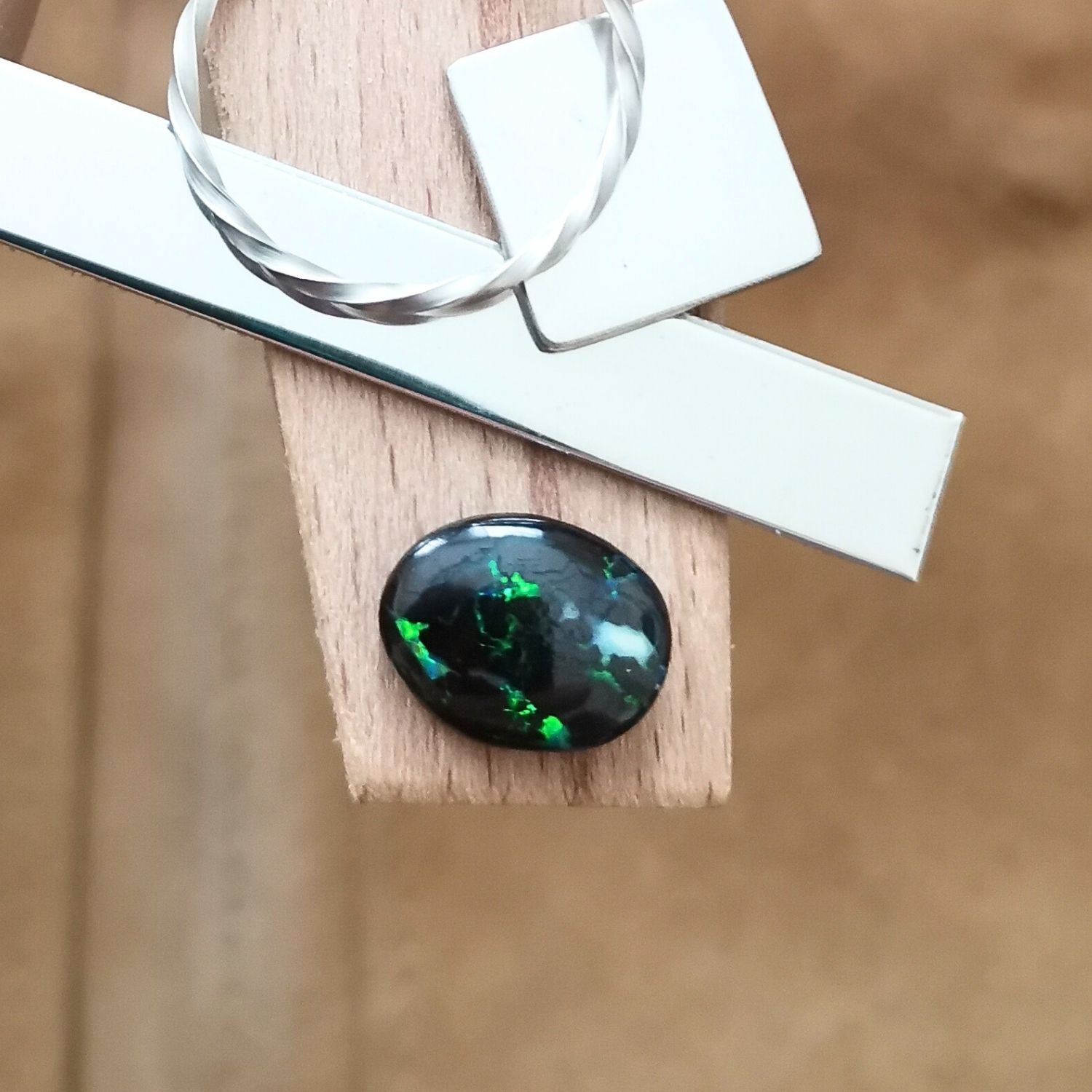 The small free-form boulder opal displayed on a jewellers bench peg with some sterling silver sheet and wire.
