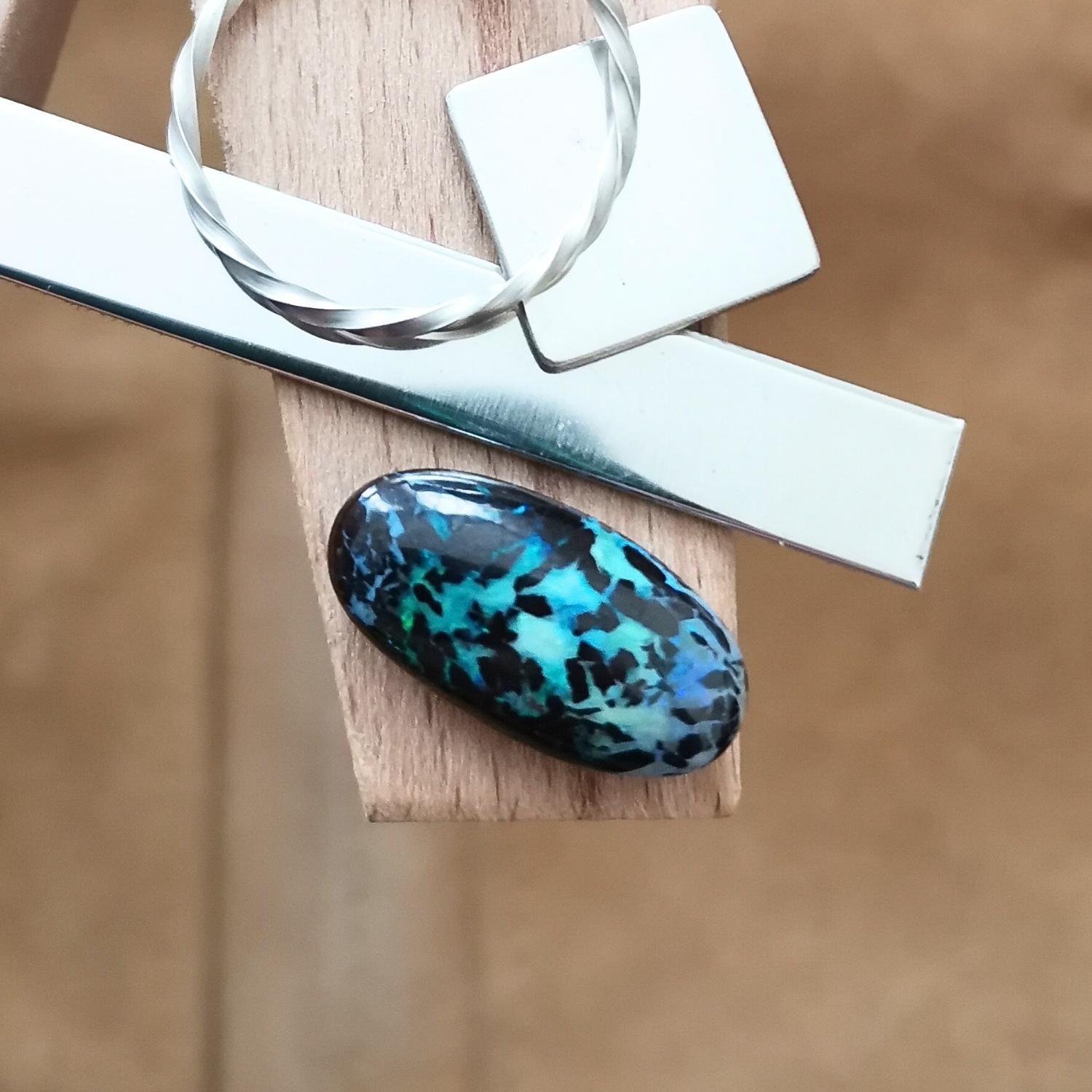 The small free-form boulder opal displayed on a jewellers bench peg with some sterling silver sheet and wire.