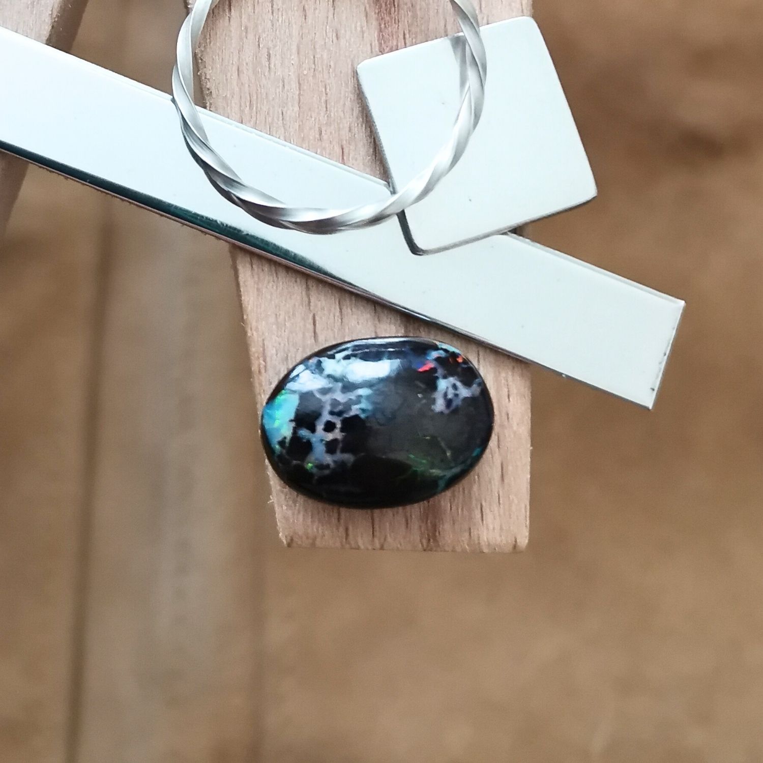 The small free-form boulder opal displayed on a jewellers bench peg with some sterling silver sheet and wire.