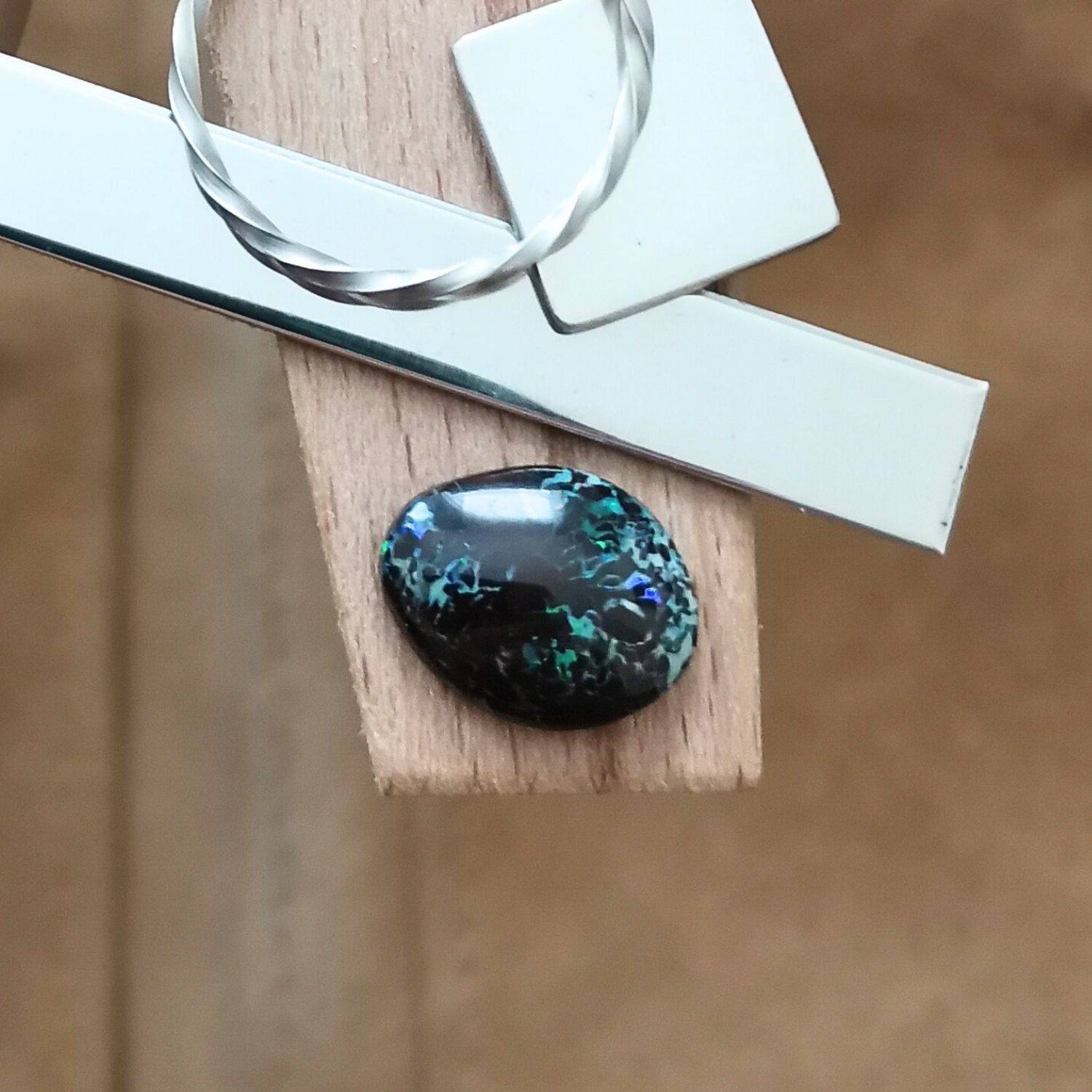 The small free-form boulder opal displayed on a jewellers bench peg with some sterling silver sheet and wire.