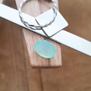The green chalcedony oval displayed on a jewellers bench peg with some sterling silver sheet and wire.