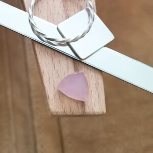 The pink chalcedony triangle displayed on a jewellers bench peg with some sterling silver sheet and wire.