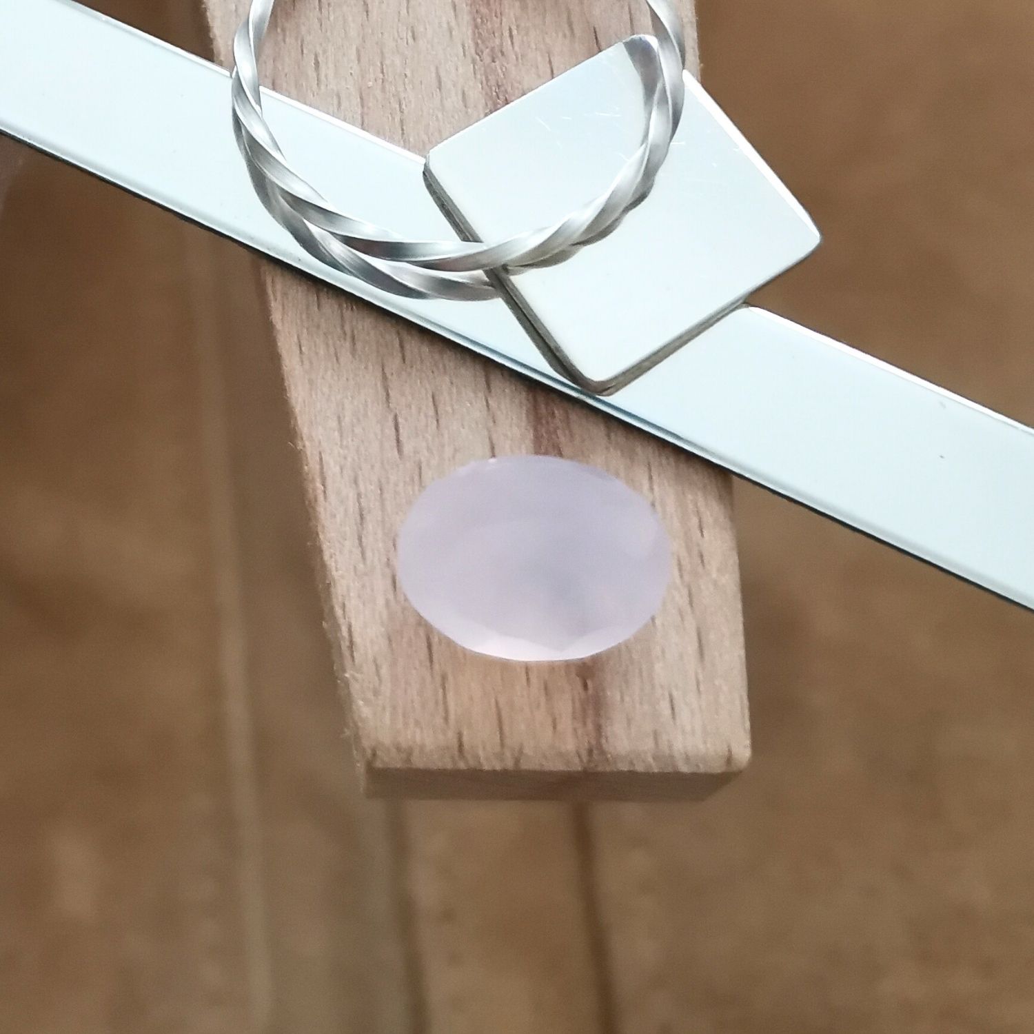 The pink rose quartz oval displayed on a jewellers bench peg with some sterling silver sheet and wire.