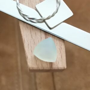 The pale chalcedony triangle displayed on a jewellers bench peg with some sterling silver sheet and wire.