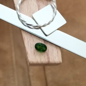 The green oval diopside displayed on a jewellers bench peg with some sterling silver sheet and wire.