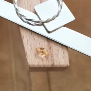 The golden yellow heliodor marquise displayed on a jewellers bench peg with some sterling silver sheet and wire.