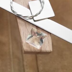 The pale yellow heliodor square displayed on a jewellers bench peg with some sterling silver sheet and wire.