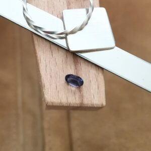 The violet iolite oval displayed on a jewellers bench peg with some sterling silver sheet and wire.