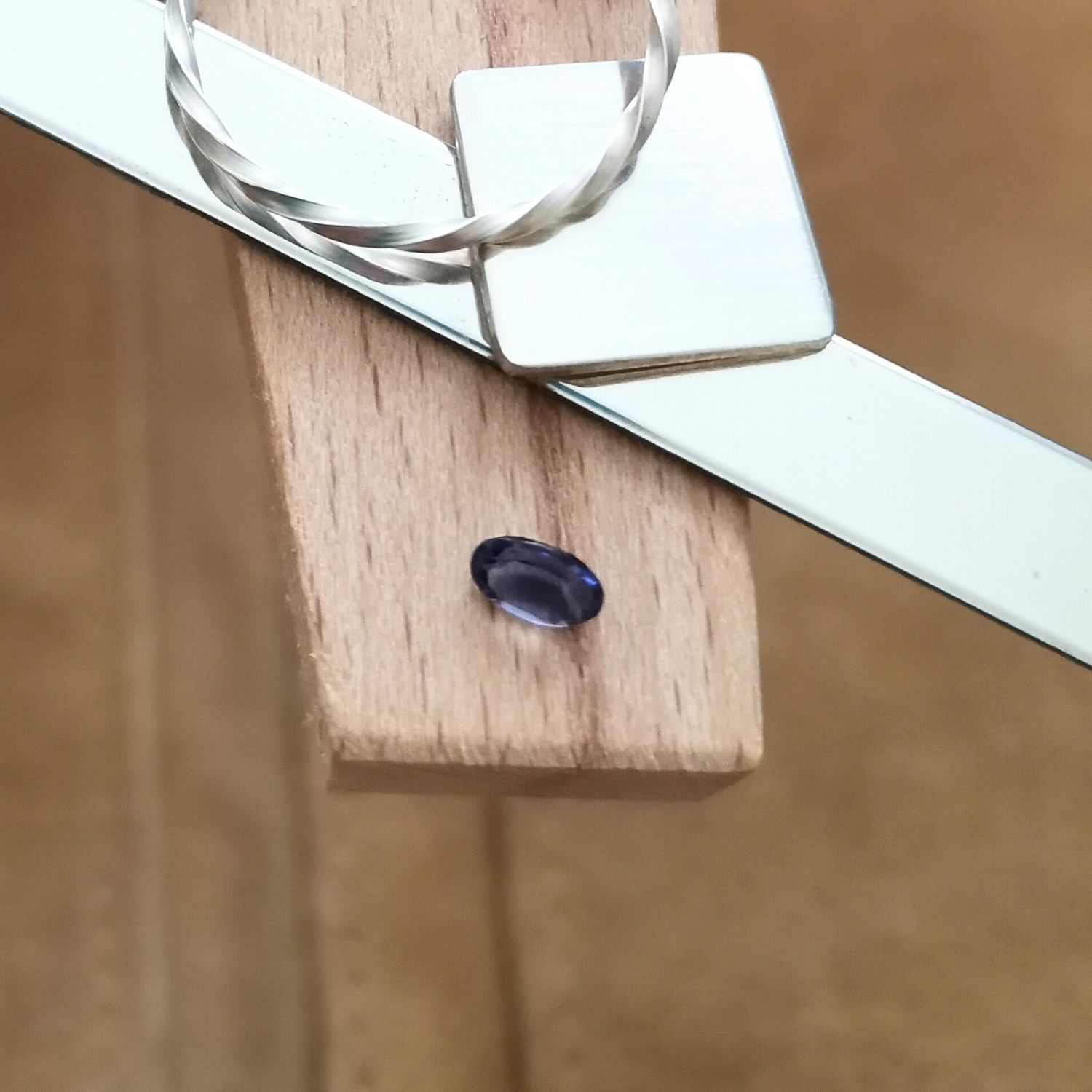 The violet iolite oval displayed on a jewellers bench peg with some sterling silver sheet and wire.