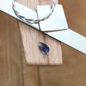 The violet iolite teardrop displayed on a jewellers bench peg with some sterling silver sheet and wire.