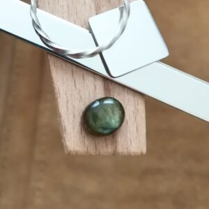 The small oval labradorite cabochon displayed on a jewellers bench peg with some sterling silver sheet and wire.