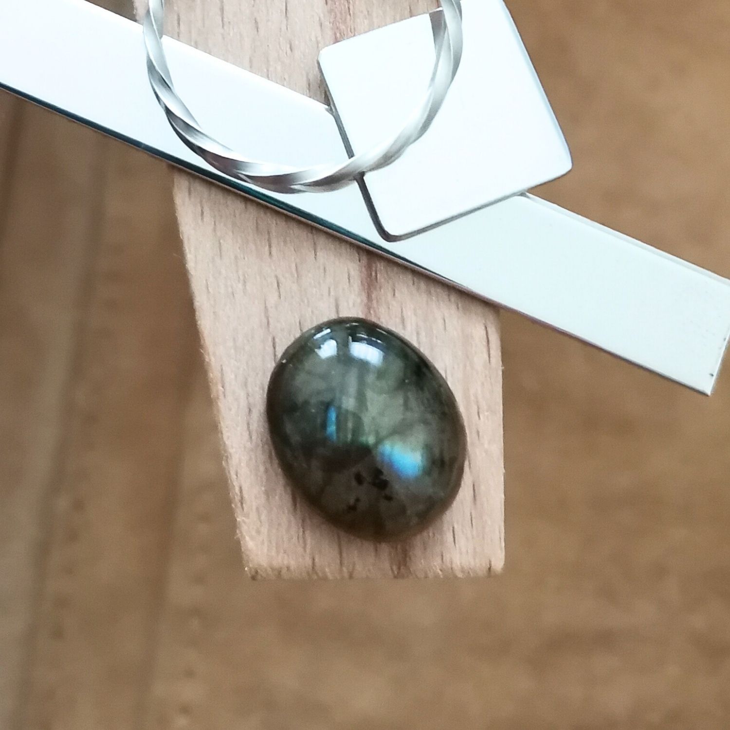 The oval labradorite cabochon displayed on a jewellers bench peg with some sterling silver sheet and wire.
